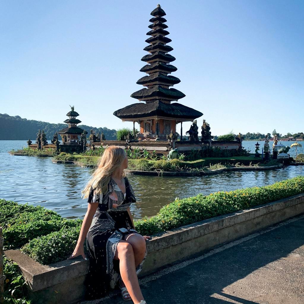 A woman enjoying the serene view of Ulun Danu Beratan Temple by the lake in sunny Bali, Indonesia.