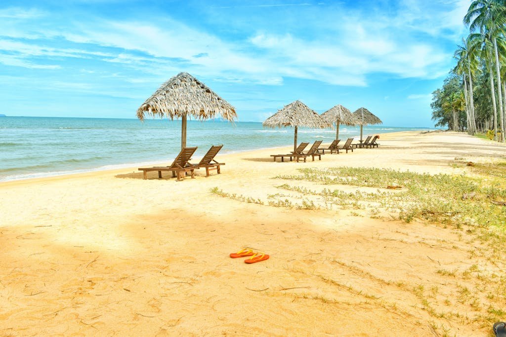 Idyllic tropical beach scene with empty lounge chairs under straw umbrellas on a sunny day.